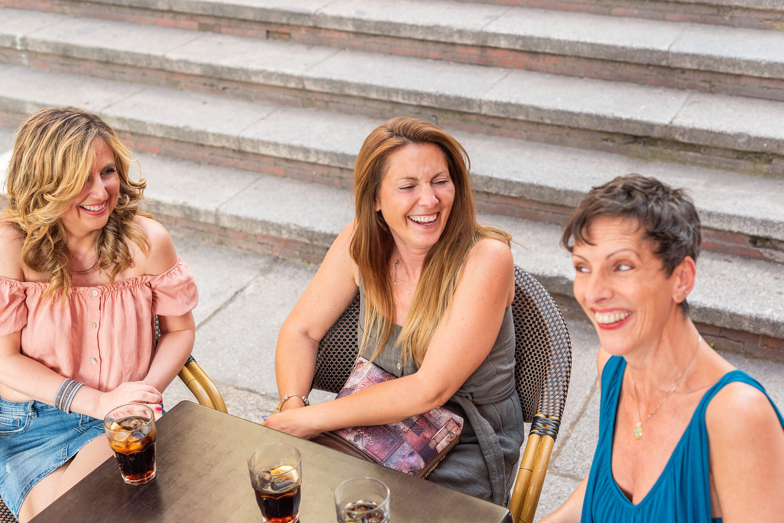 Three adult women in a cafe outside laughing and having drinks. High angle view of beautiful mature women having a good time together.